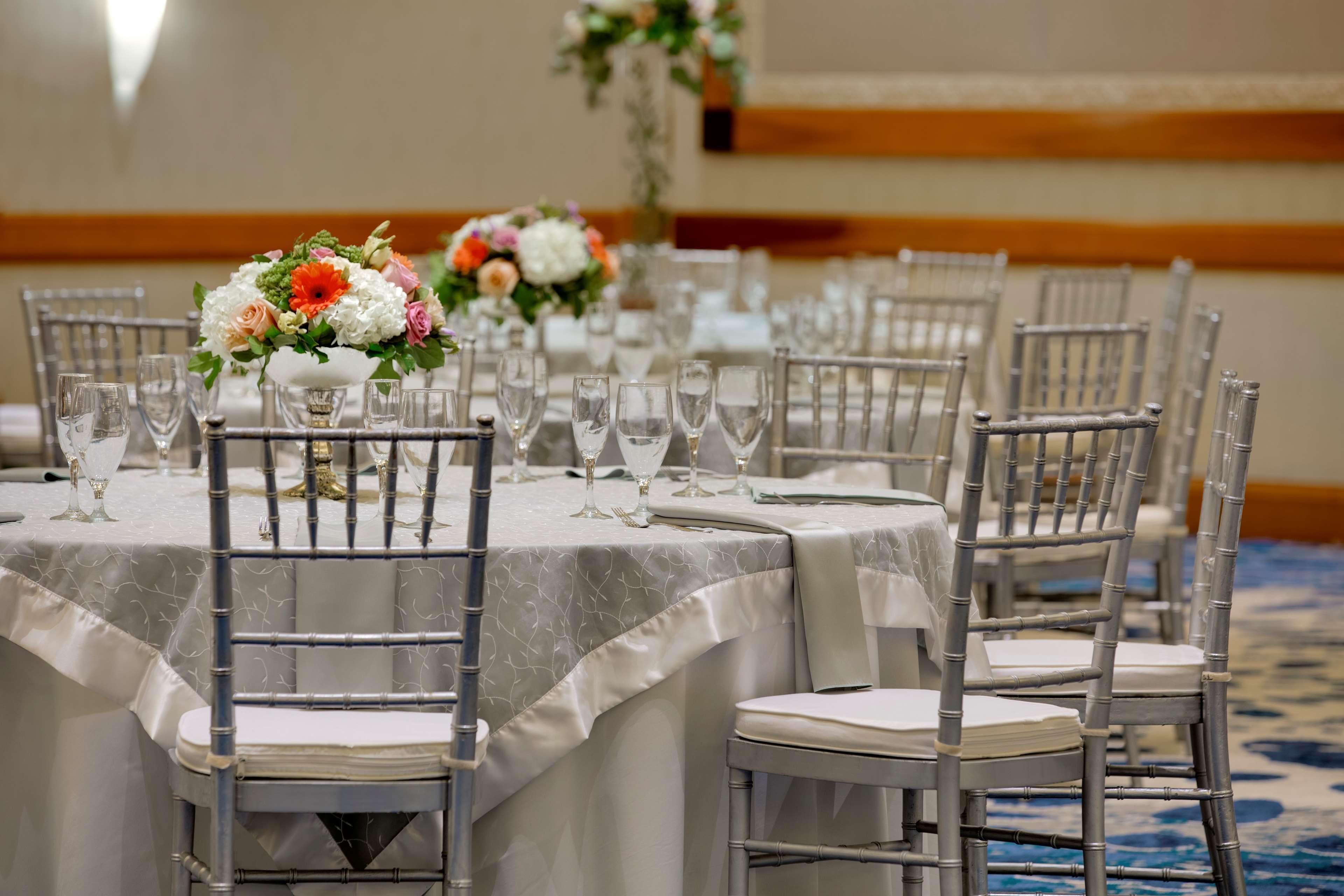 A banquet hall with round tables, each set with chairs, wine glasses, and floral centerpieces.