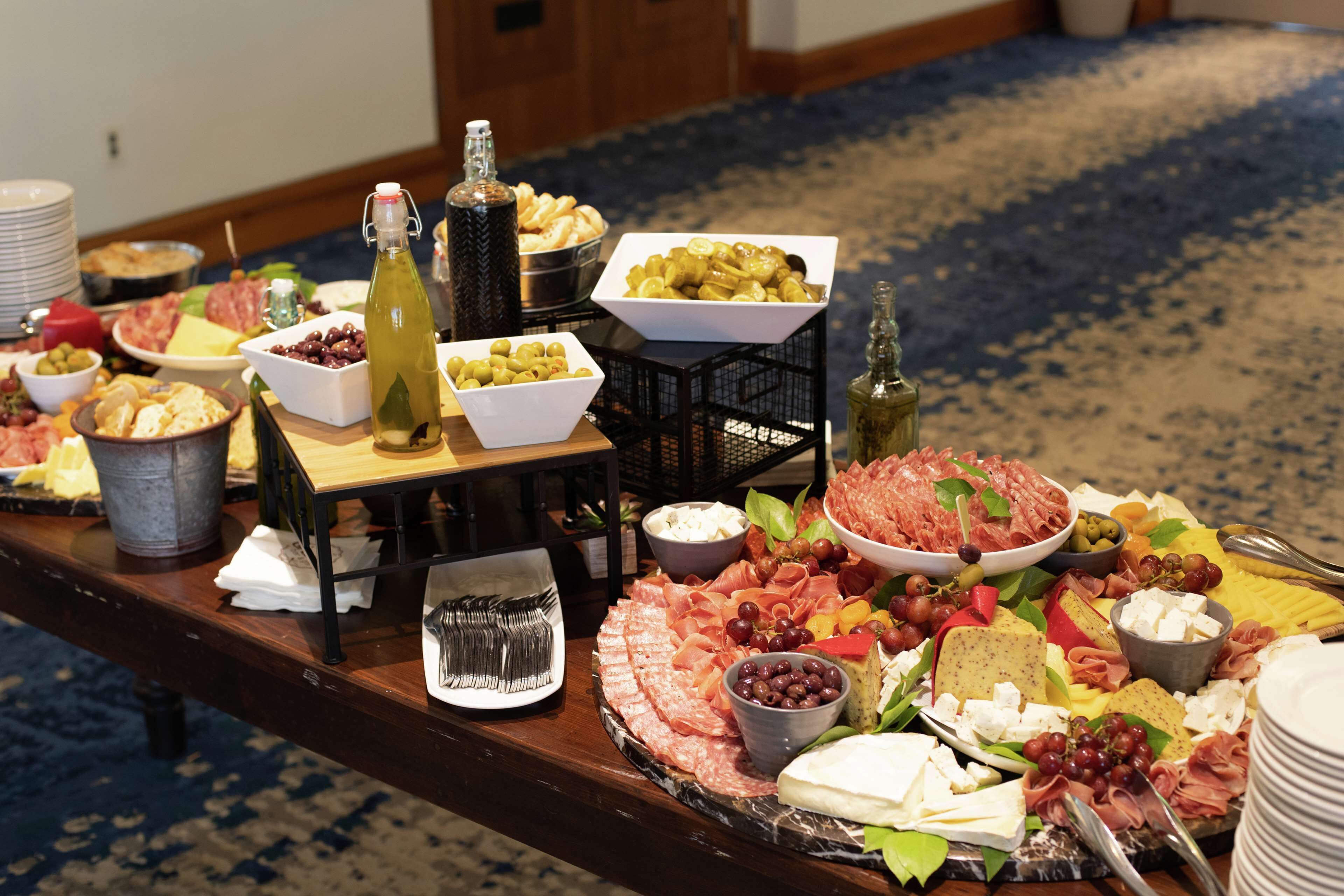 A buffet table with various cheeses, meats, olives, and grapes.