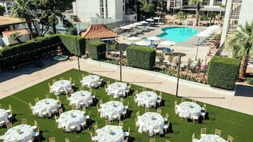 Un pati d'hotel amb diverses taules rodones preparades per dinar, una piscina i una zona de jardí paisatjística.