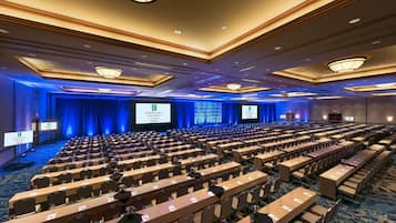 Una sala conferenze con file di tavoli e sedie, un palco con schermo e un tappeto blu.