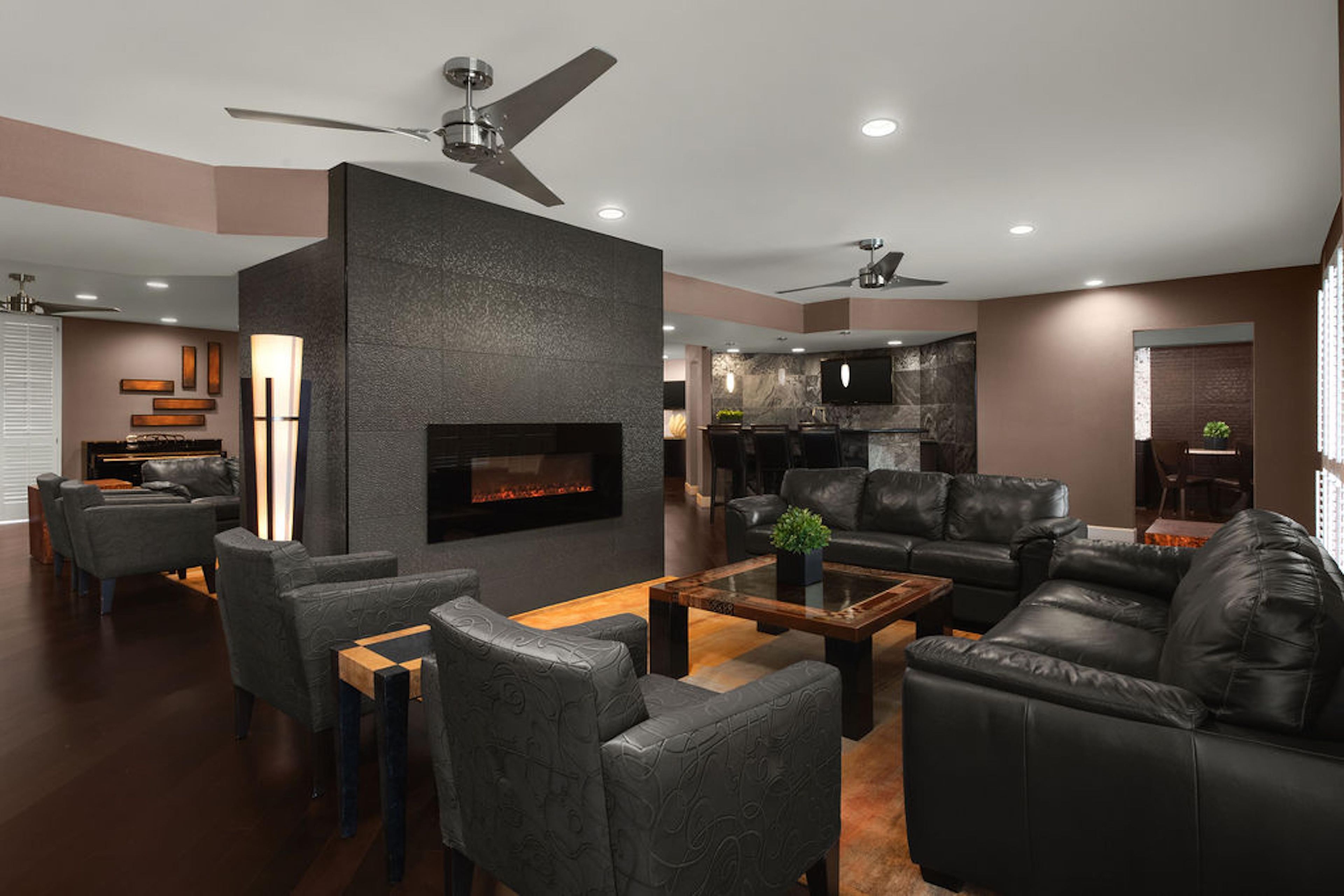A modern living room with a fireplace, leather sofas, and a dining area with a kitchen in the background.