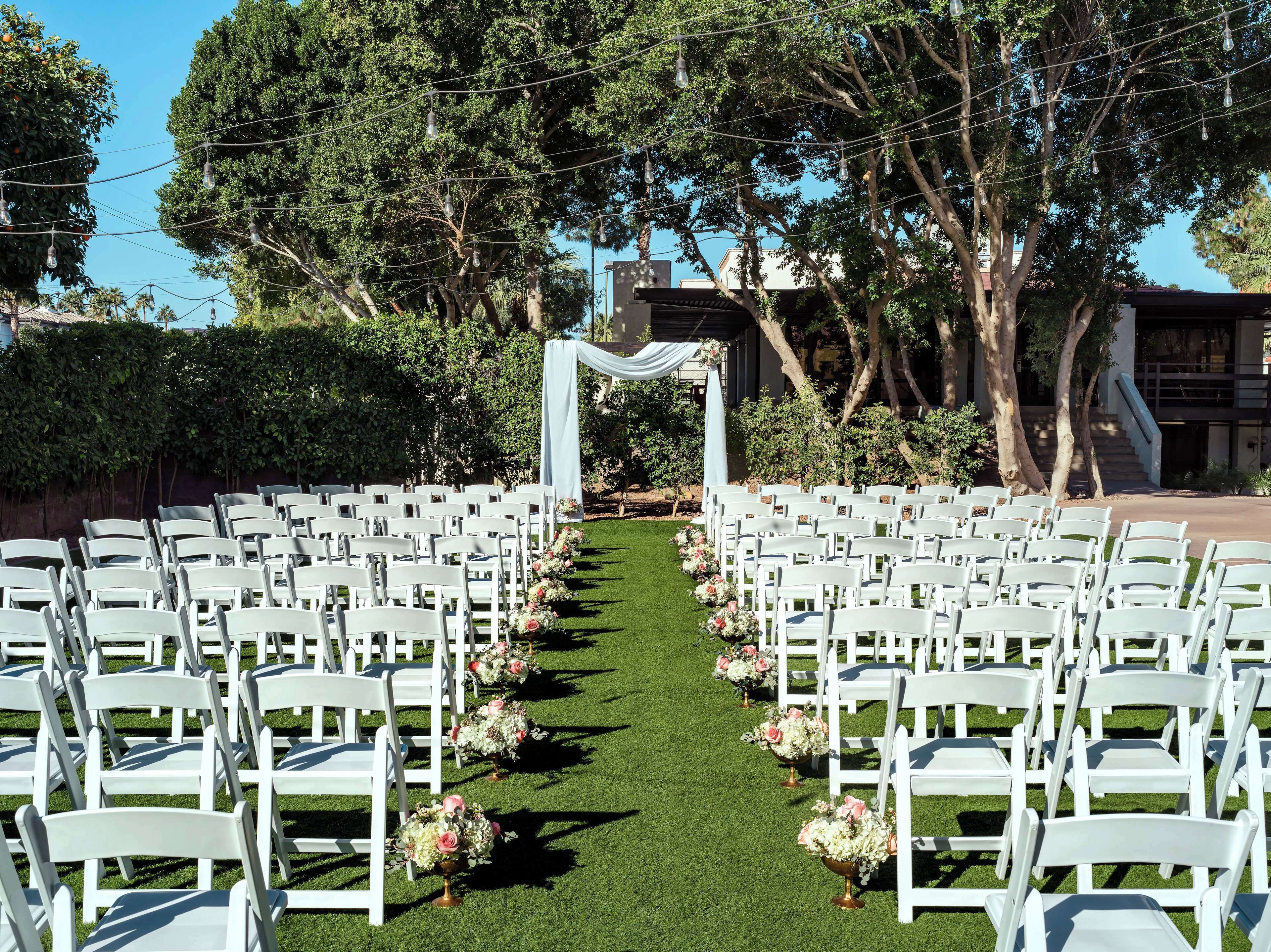 An outdoor wedding venue with rows of white chairs and a green carpet aisle.