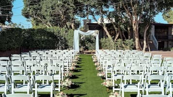 Un lieu de réception en plein air pour les mariages, avec des rangées de chaises blanches et une allée recouverte d’une moquette verte.