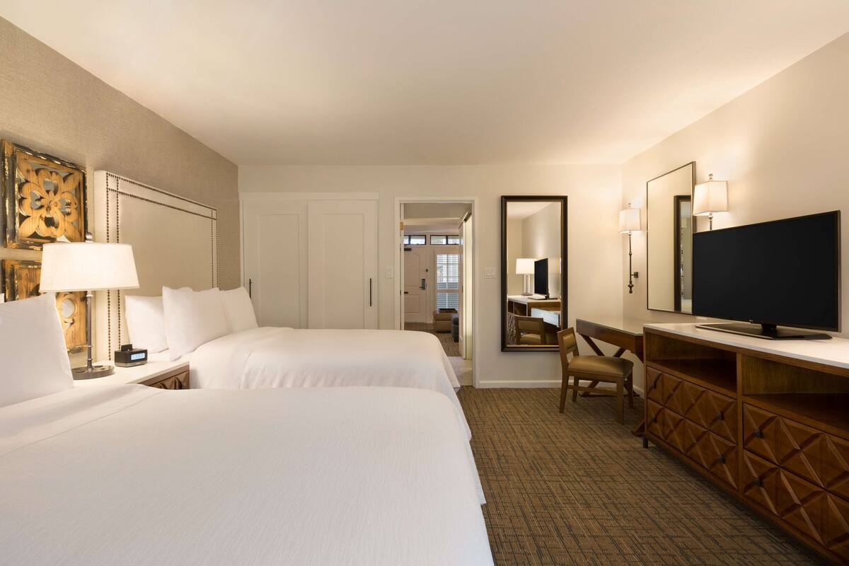 A hotel room with two beds, a TV, a desk, and a mirror.
