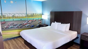 Et hotelværelse med en stor seng, et natbord, en lampe og et vægmaleri af en racerbane.
