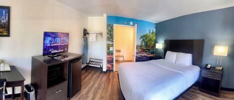 A hotel room with a bed, a desk with a television, a microwave, and a nightstand with a lamp.