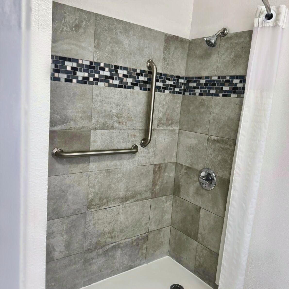 A shower area with a tiled wall, a grab bar, a showerhead, and a curtain.