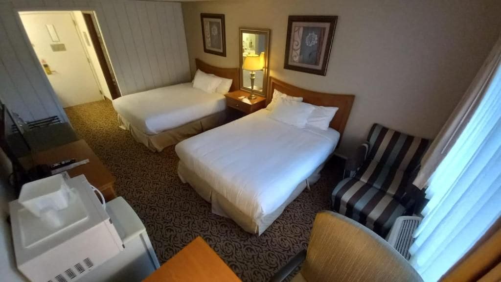 A hotel room with two beds, a desk, a chair, and a window.