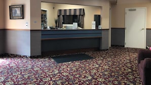 A hotel reception area with a reception desk, a large mirror, a telephone, a framed picture, and a door.