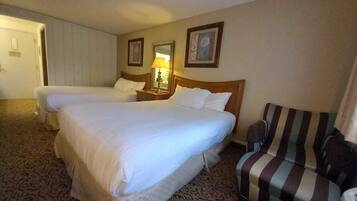 A hotel room with two beds, a striped armchair, a bedside table with a lamp, and patterned carpet.