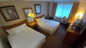 A hotel room with two beds, a desk, a chair, and a small seating area.