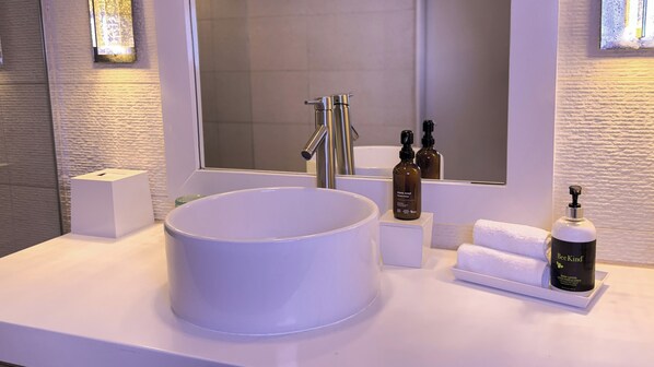 Un baño con un lavamanos grande de color blanco, un espejo y dos botellas de jabón para manos.
