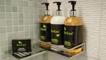 A bathroom shelf with three bottles of BeeKind products and a box of BeeKind facial bar.