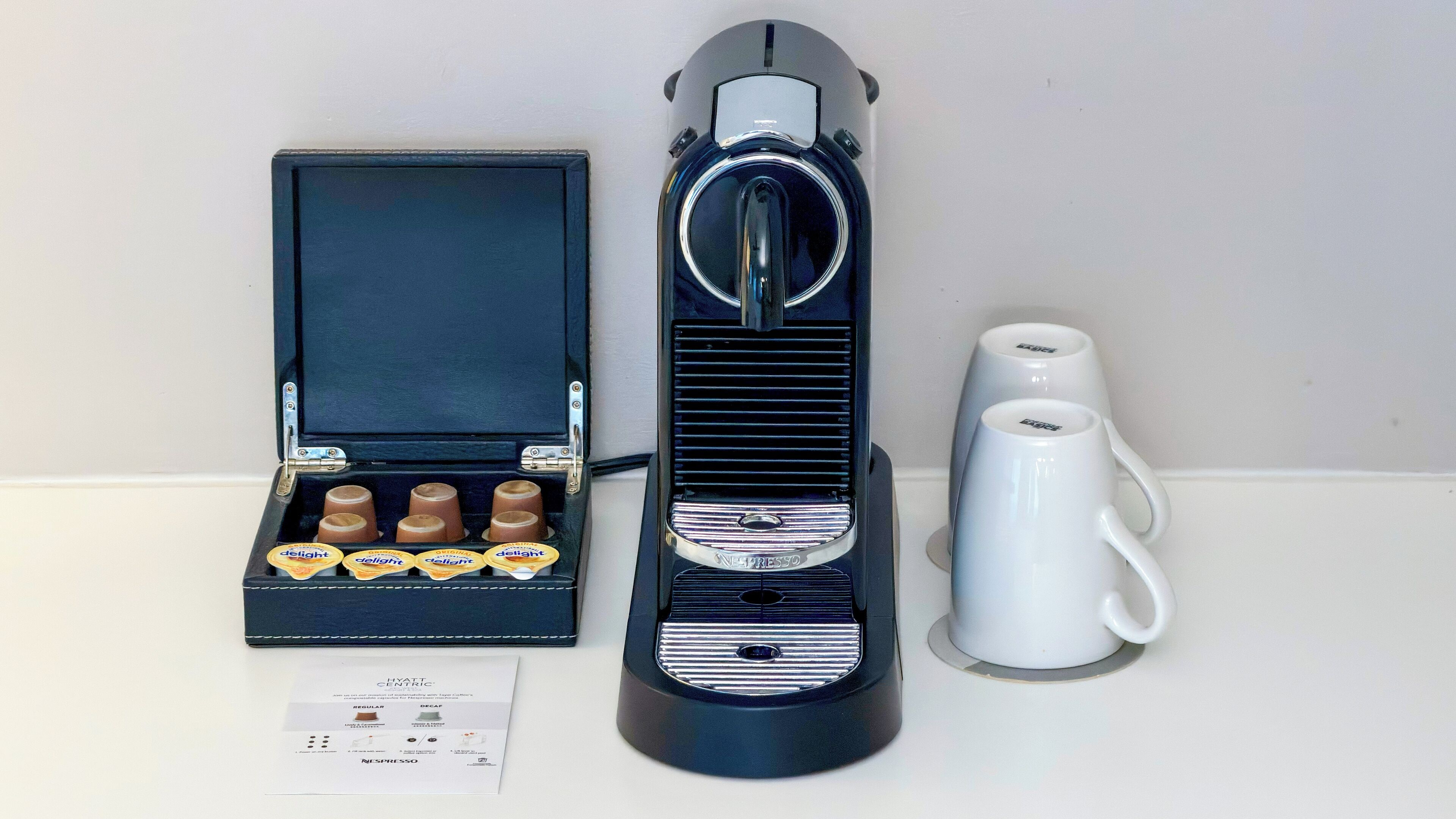 Une machine à café, une boîte de dosettes de café et une tasse blanche.