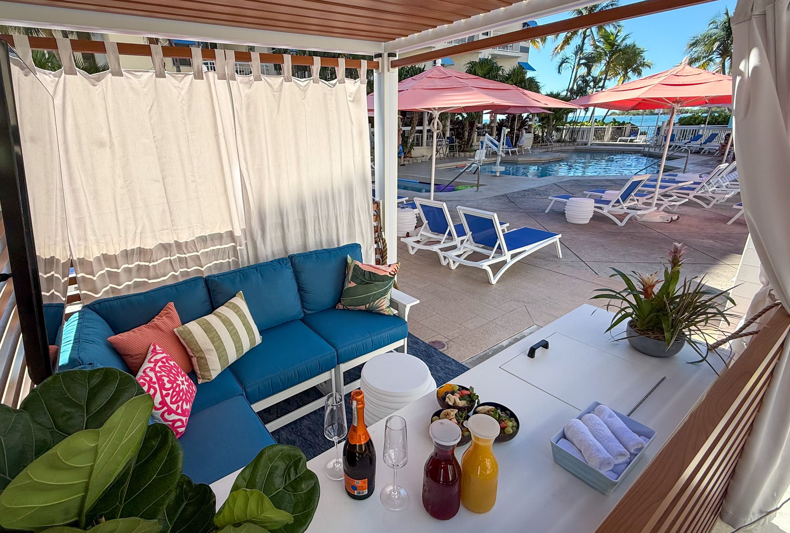 A poolside area with a blue sofa, lounge chairs, and a table with drinks and snacks.
