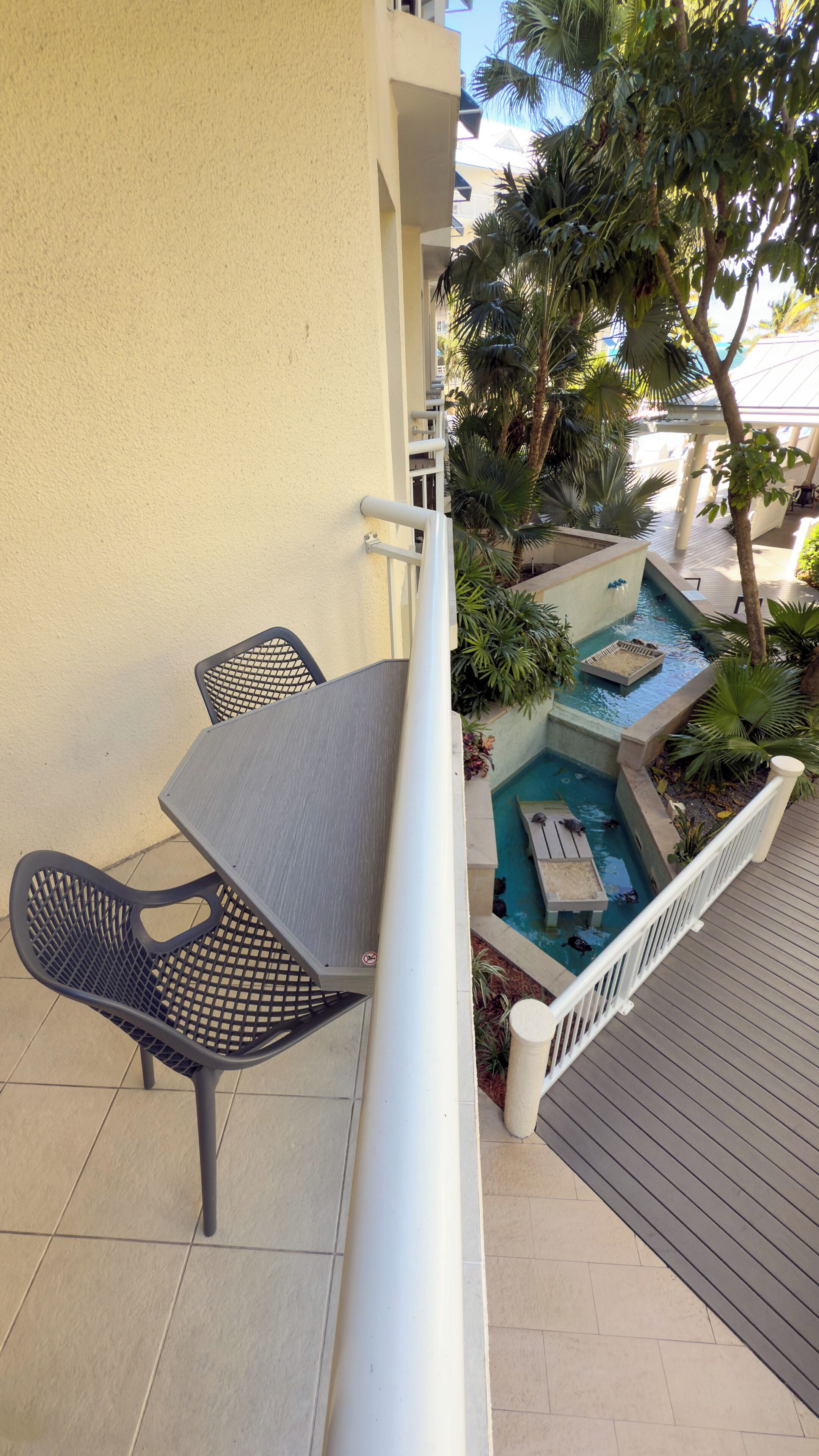 Un balcon avec une table et des chaises, un petit espace piscine avec une terrasse en bois et une rambarde blanche.