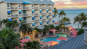 A hotel with multiple balconies, a swimming pool, and palm trees.