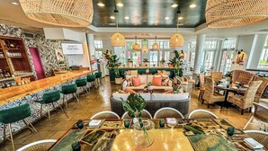 A spacious bar area with a wooden counter and green bar stools, a seating area with a sofa and chairs, and a dining area with a table set for two. - Hyatt Centric Key West Resort and Spa (Key West)