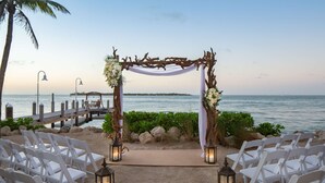 A beach wedding setup with white chairs, a wooden arch, and lanterns.