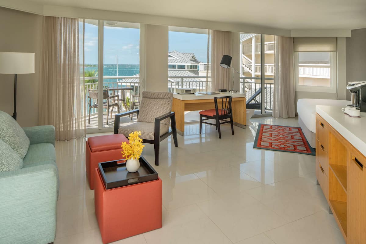 A modern hotel room with a balcony, a dining area, and a kitchen.