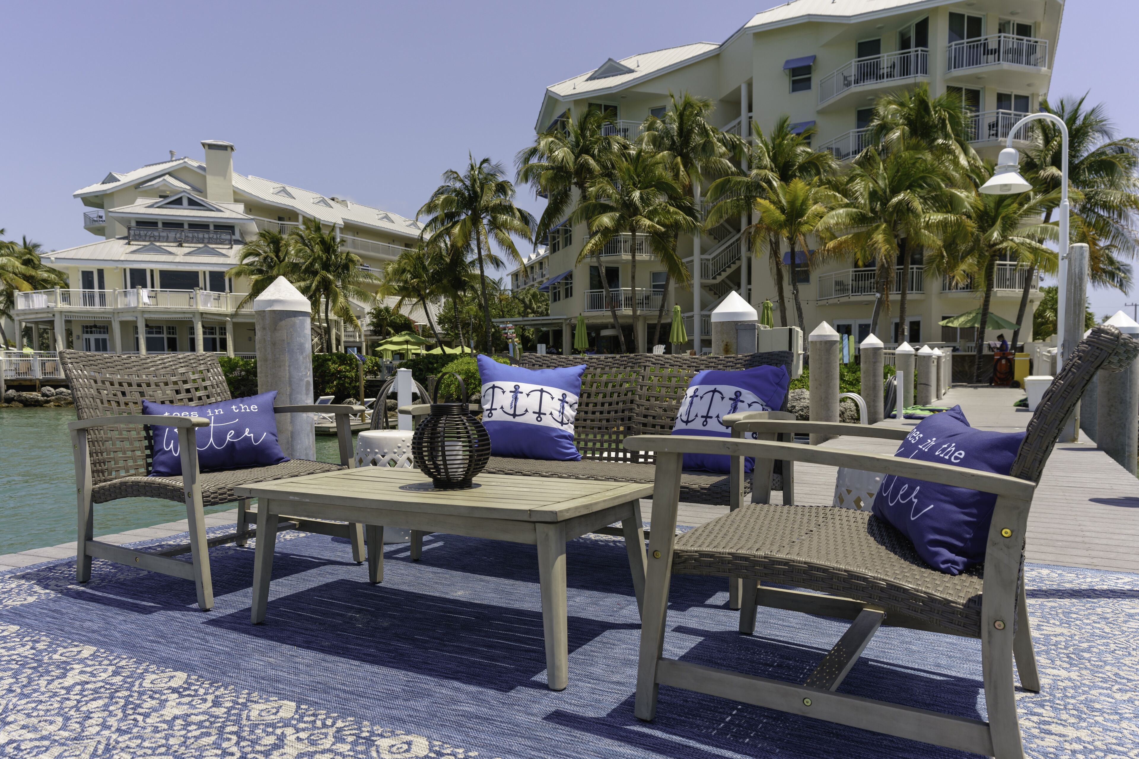 A deck with wicker furniture, a table, and a vase with a plant.