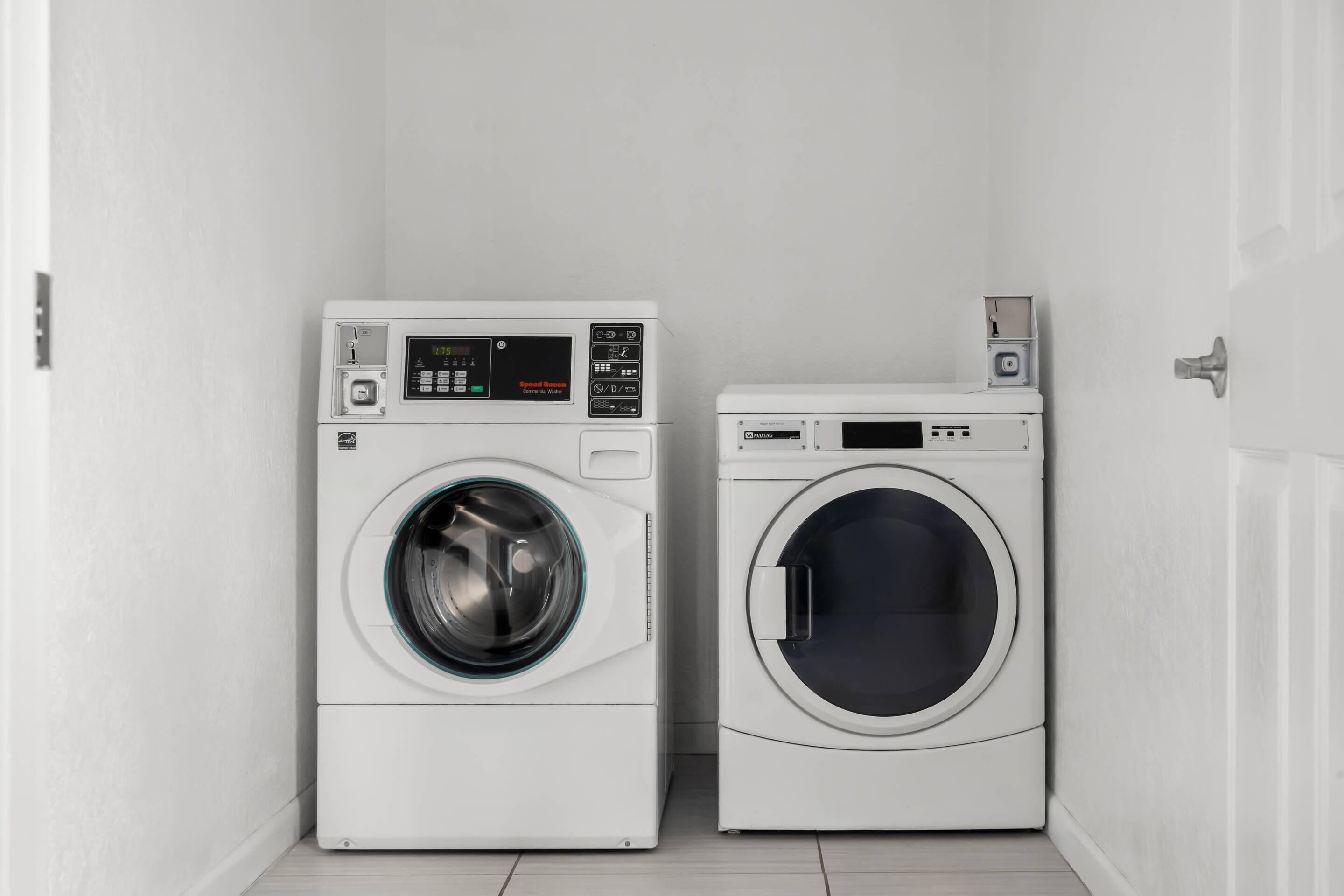 Two front-loading washing machines in a corner of a room with white walls and a tiled floor.