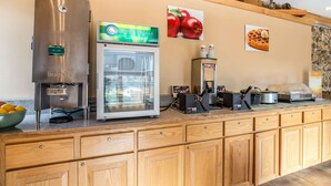 A kitchen area with a stainless steel refrigerator, a glass display case, a waffle maker, and a coffee station.