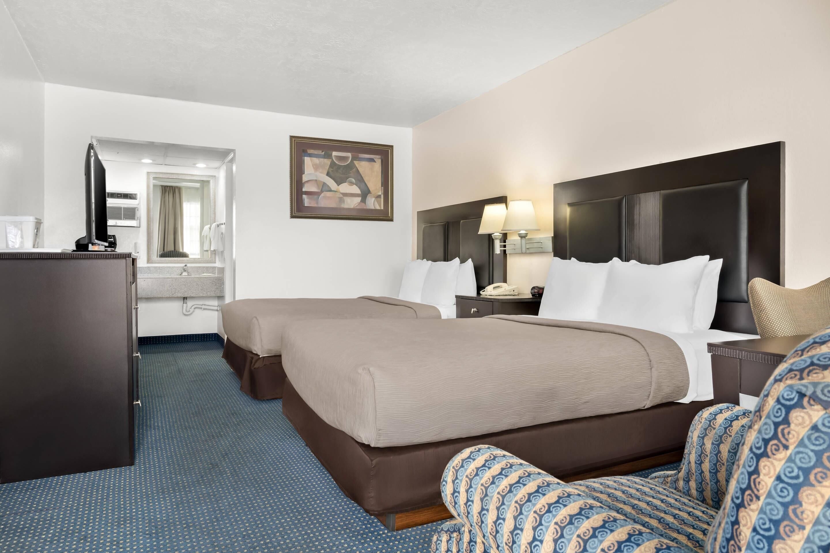 Ett hotellrum med två sängar, ett skrivbord, en stol och en tavla på väggen.