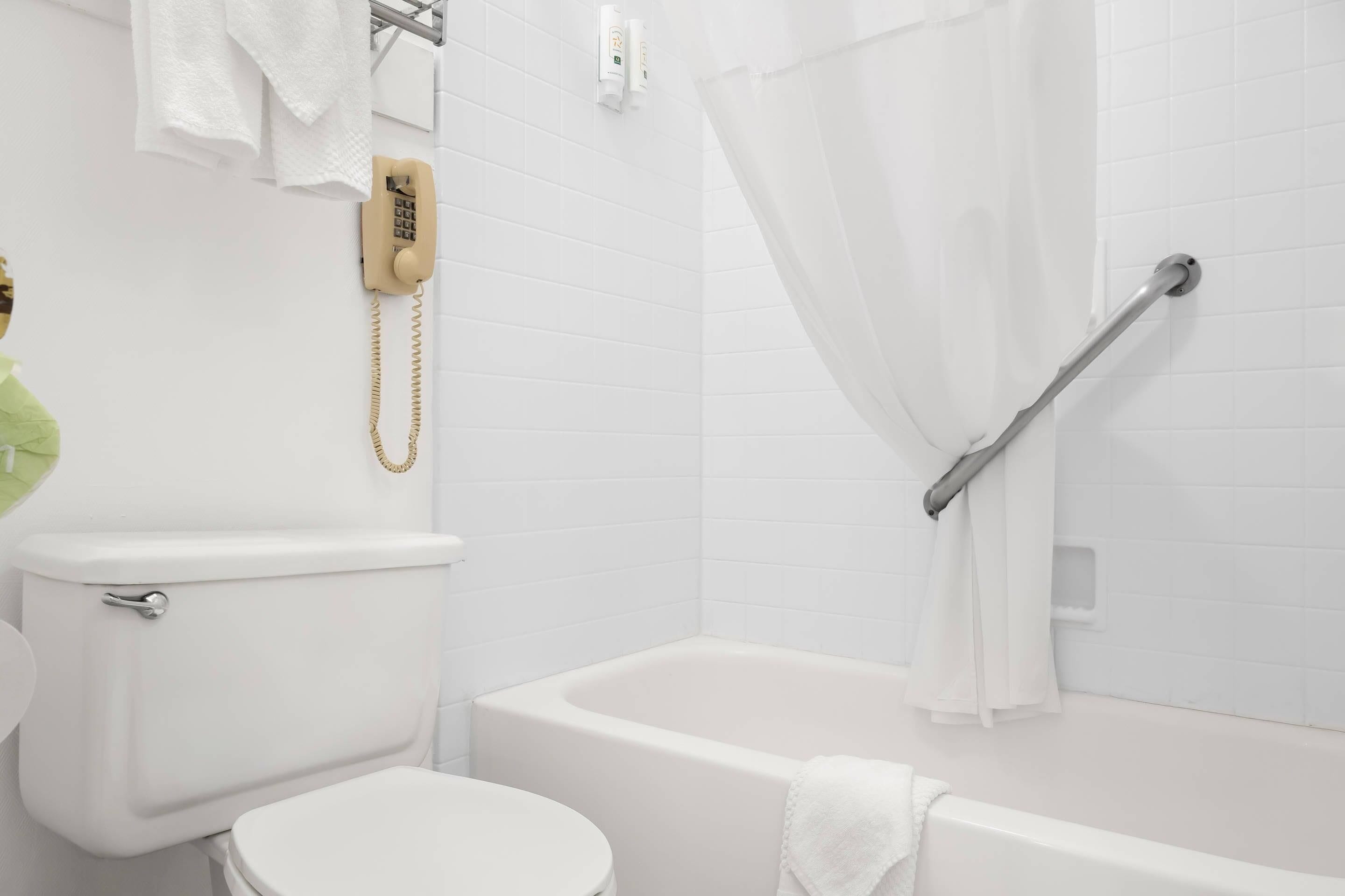 Ein Badezimmer mit Toilette, einer Badewanne, einer Dusche mit Haltegriff und einem Telefon.