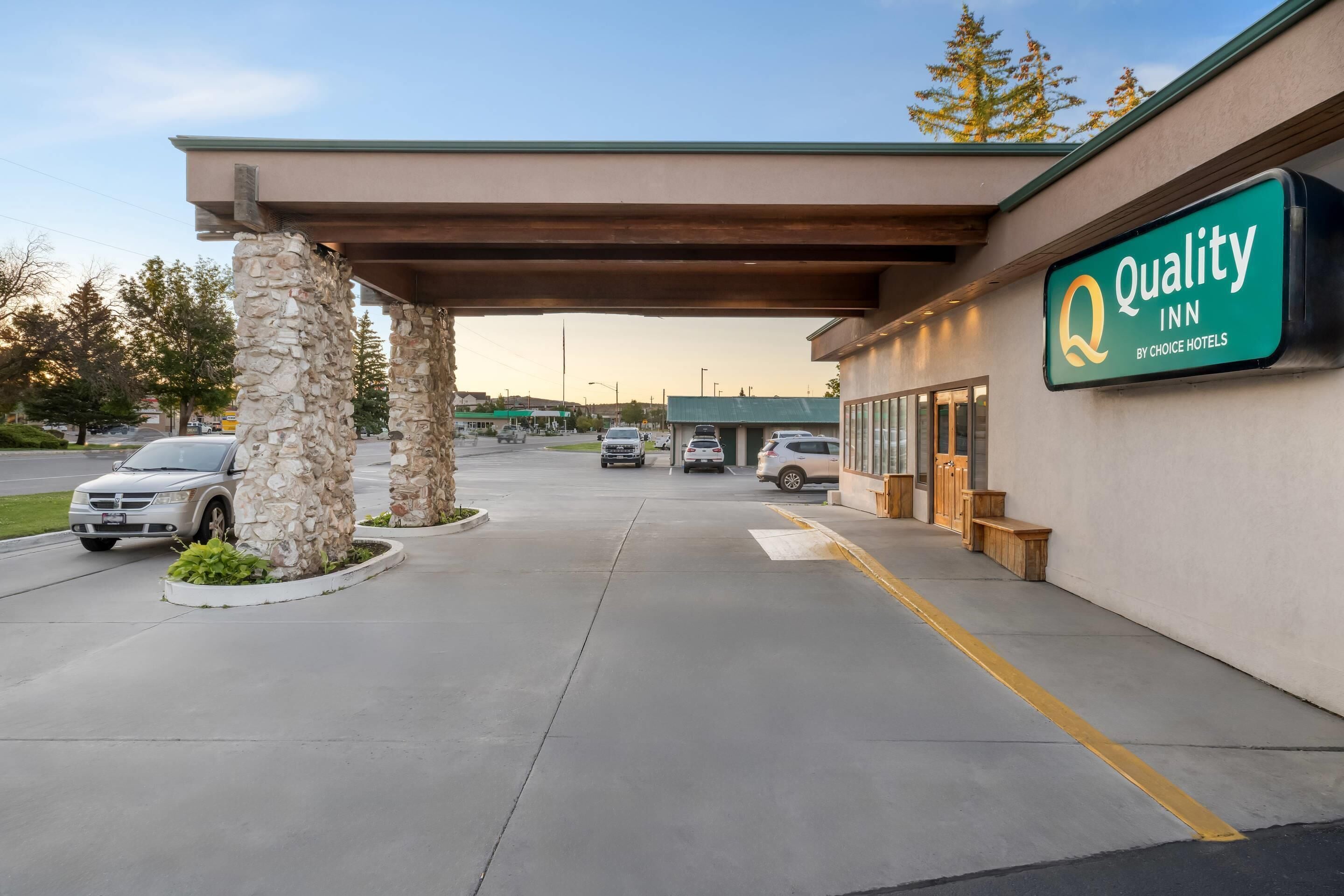 Quality Inn by Choice Hotels com entrada por pilares de pedra, área de estacionamento coberta e céu claro.