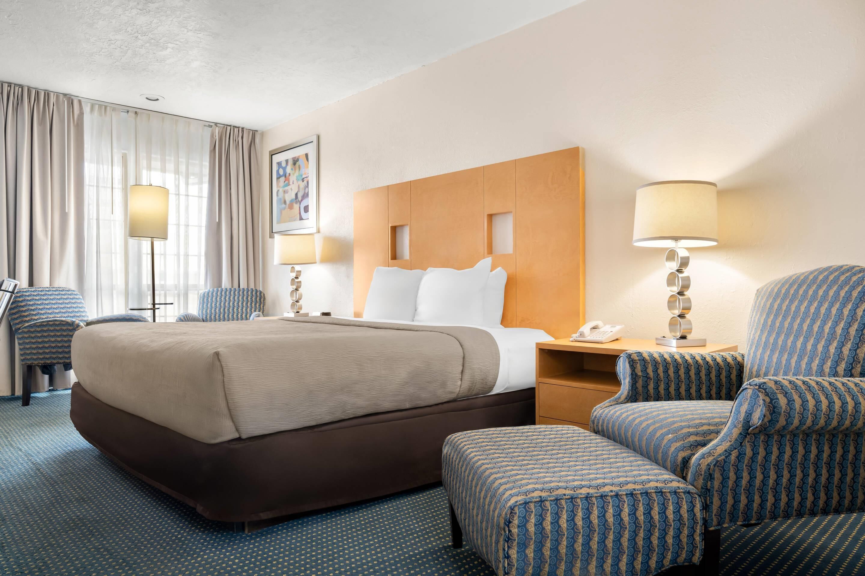 A hotel room with a large bed, two armchairs, a desk with a phone, and a wall-mounted lamp.