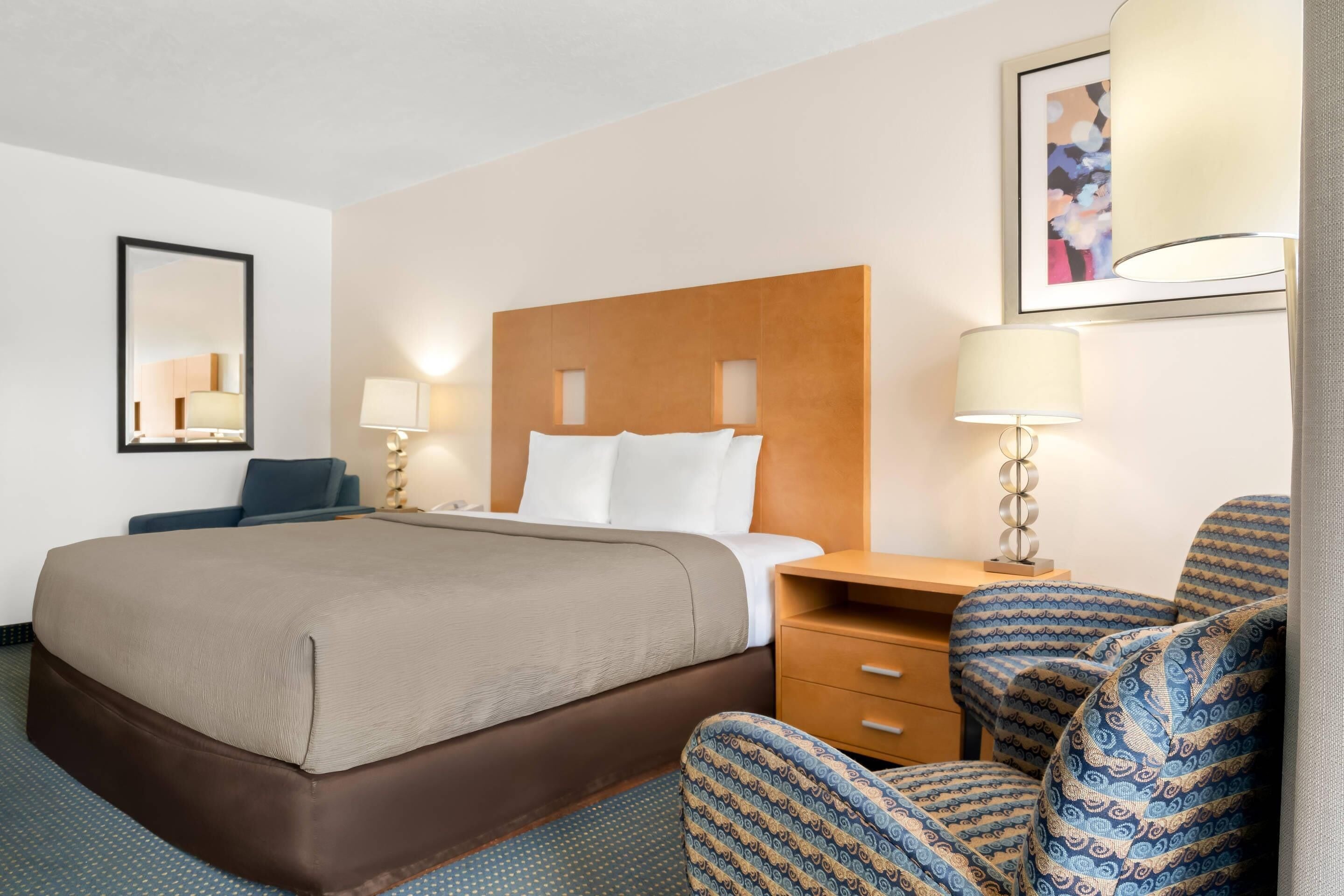 Una habitación de hotel con una cama, dos mesitas de noche, una silla, un escritorio y un espejo.