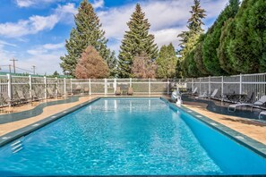 A rectangular swimming pool with clear blue water, surrounded by a white fence, and trees in the background.