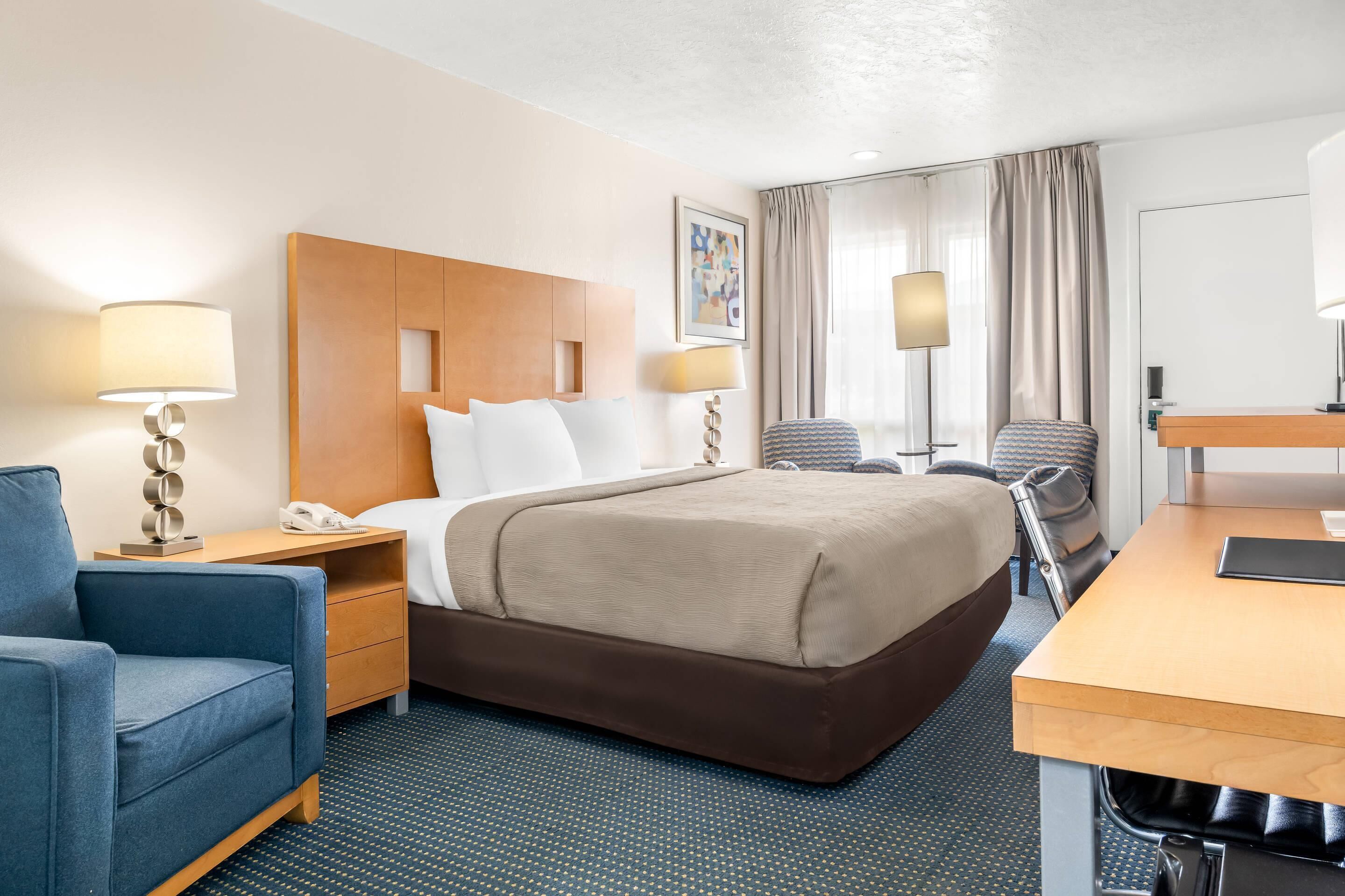A hotel room with a bed, a desk, a chair, a lamp, and a phone.