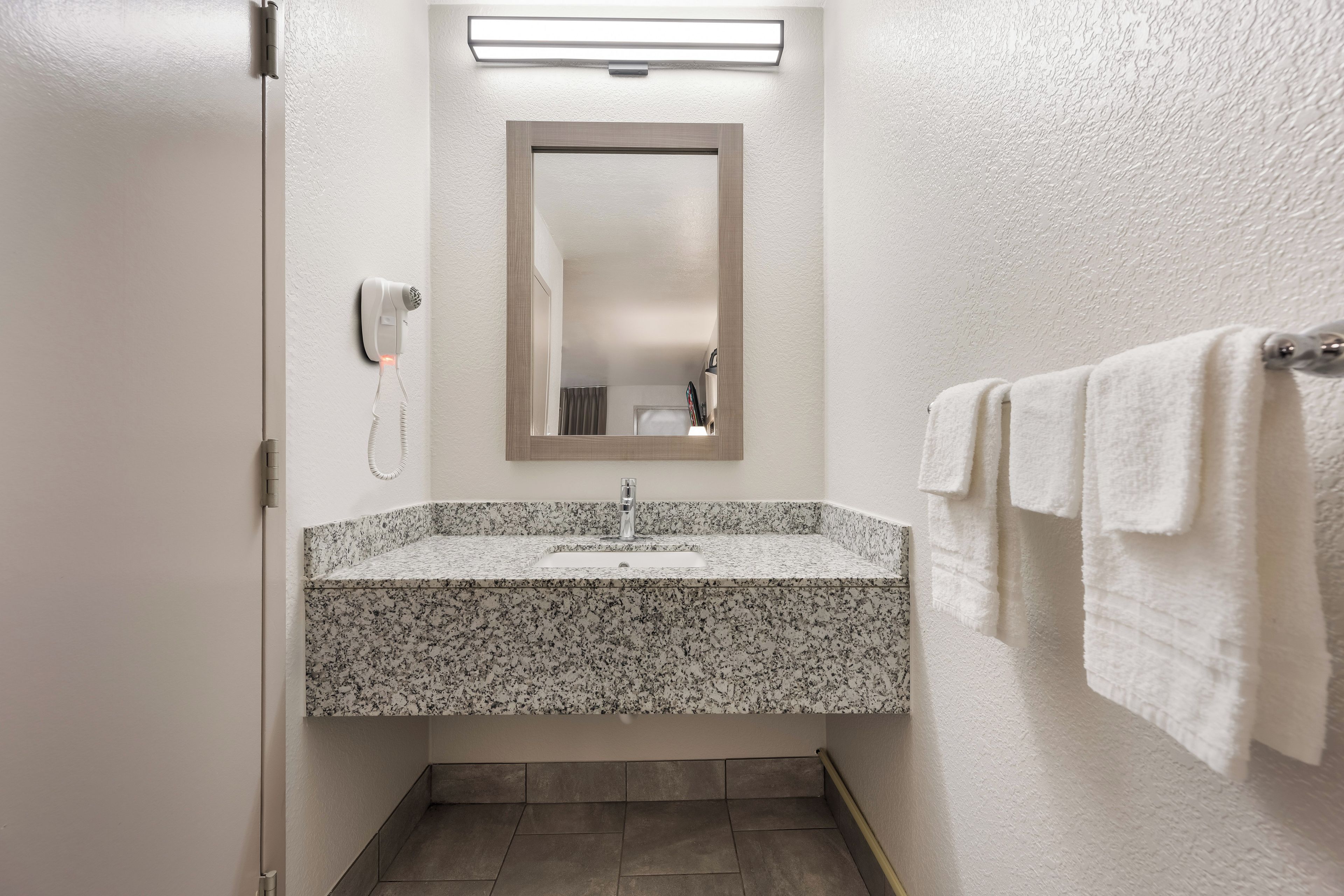 Baño con lavamanos de encimera de granito, espejo, secador de pelo y toallero.