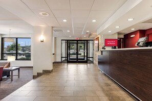 A hotel reception area with a reception desk, a sign indicating free Wi-Fi, and a view of the parking lot through the glass doors. - Red Roof Inn Birmingham South (Birmingham)