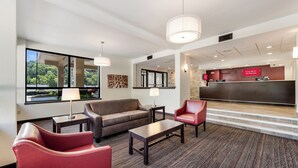 A hotel lobby with a reception desk, a sofa, a red chair, and a lamp. - Red Roof Inn Birmingham South (Birmingham)