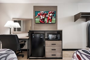 A hotel room with a flat-screen TV mounted above a desk, a microwave, a refrigerator, a chair, and a bed with striped bedding. - Red Roof Inn Birmingham South (Birmingham)