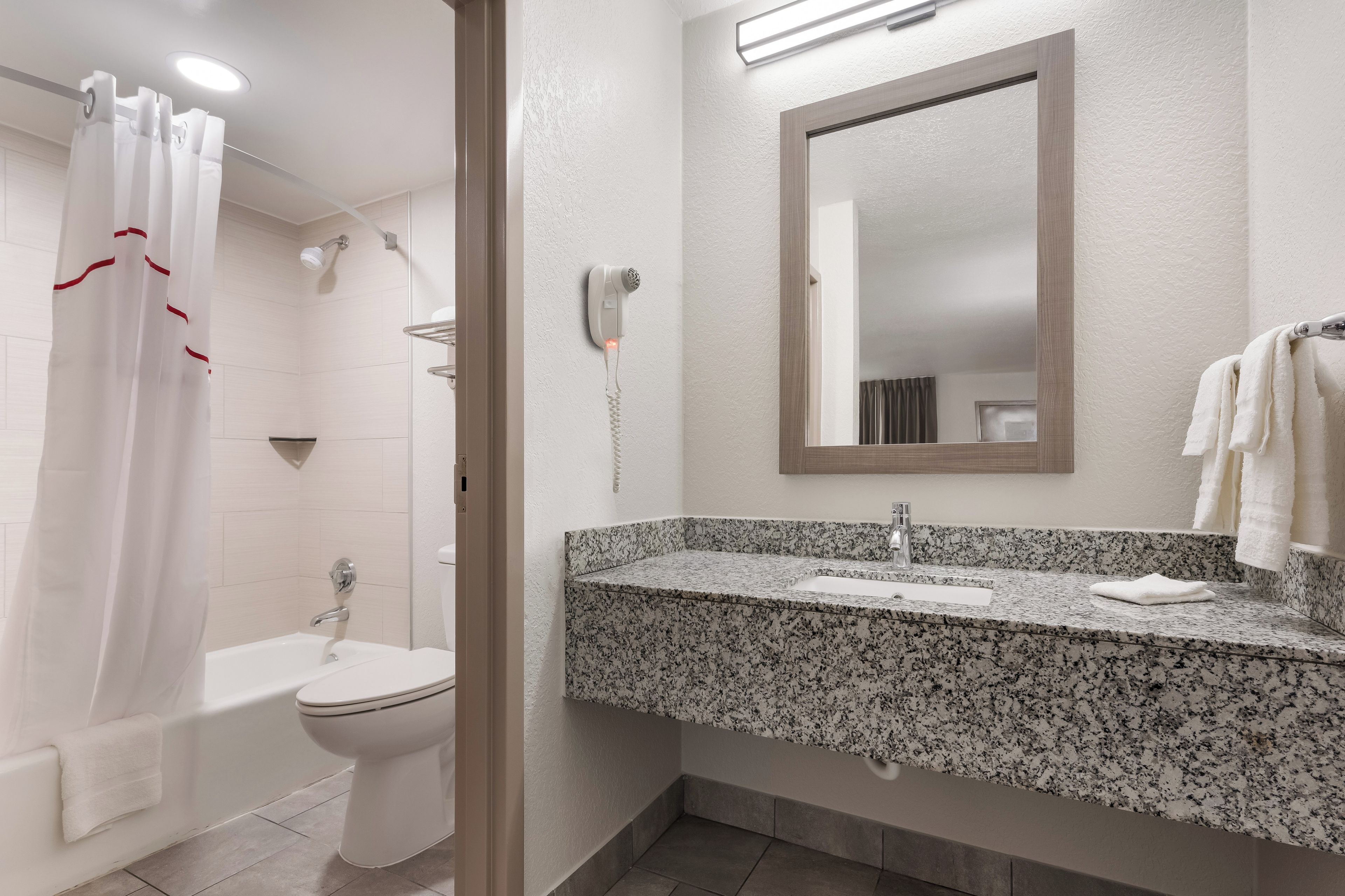 Un baño con ducha, inodoro y lavamanos con encimera de granito.
