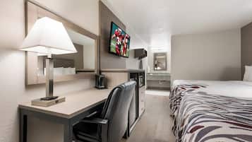 A hotel room with a desk, chair, bed, TV, and a coffee maker.