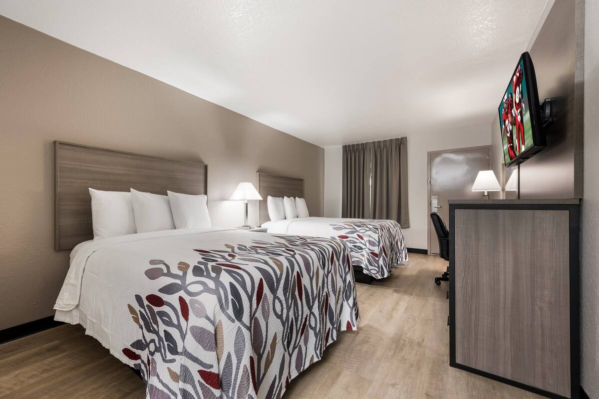 Een hotelkamer met twee bedden, een televisie, een bureau en een stoel.