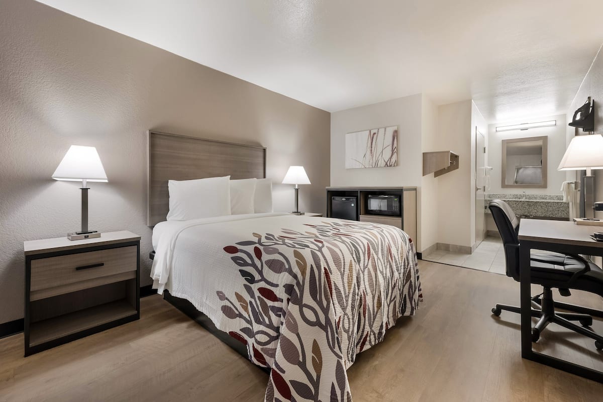 A hotel room with a bed, bedside tables, a desk, and a chair.