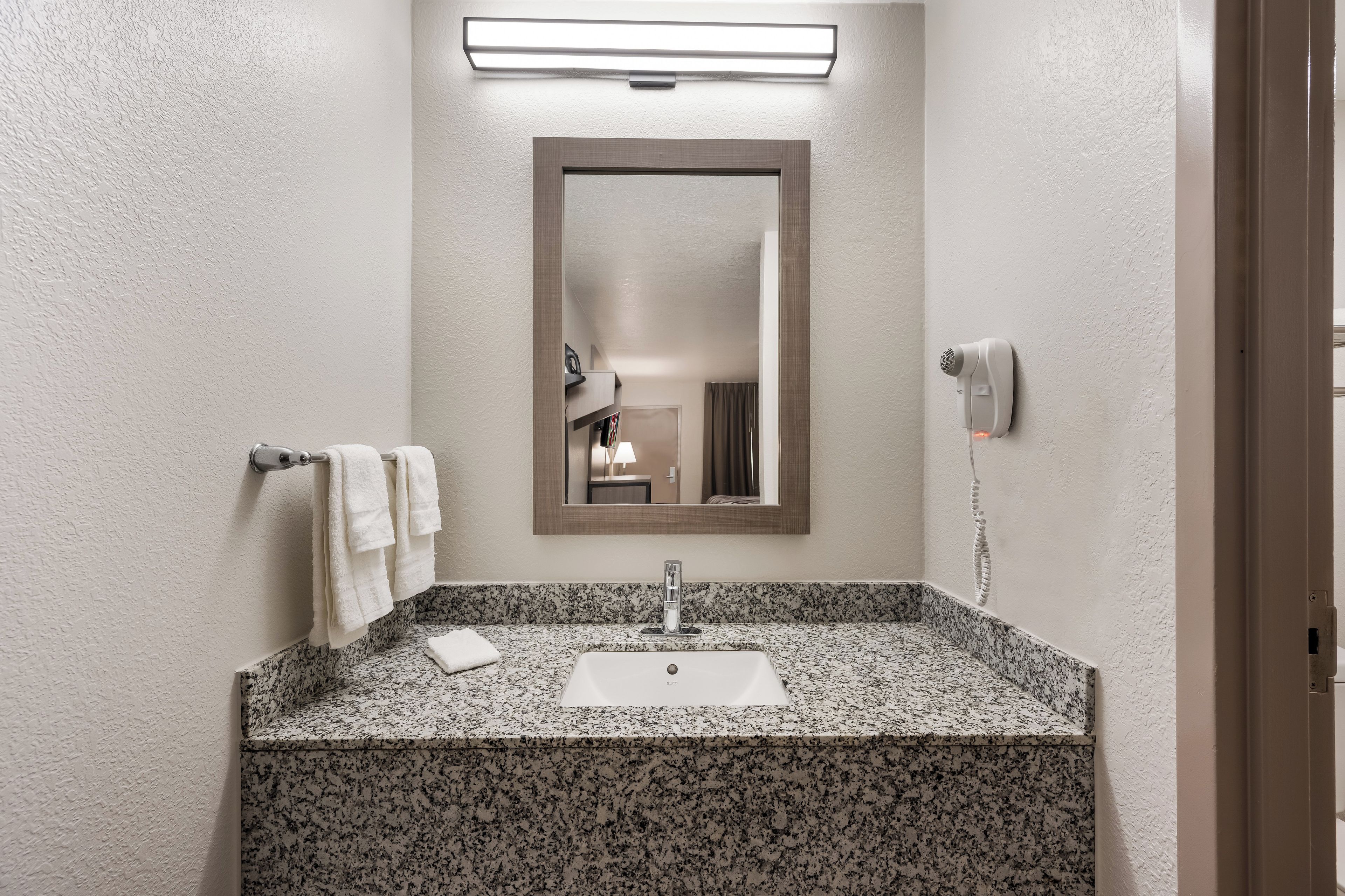 A bathroom with a granite countertop, a white sink, a mirror, and a towel rack.