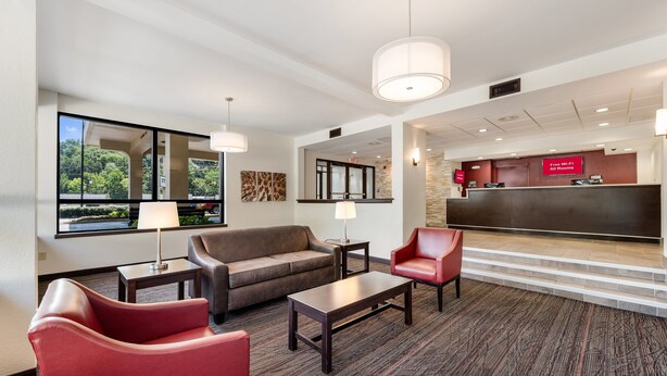 Un hall de hotel con una mesa de recepción, un sofá, una silla roja y una lámpara.