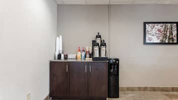 A kitchenette with a coffee maker, sugar dispenser, and coffee creamer on the counter.