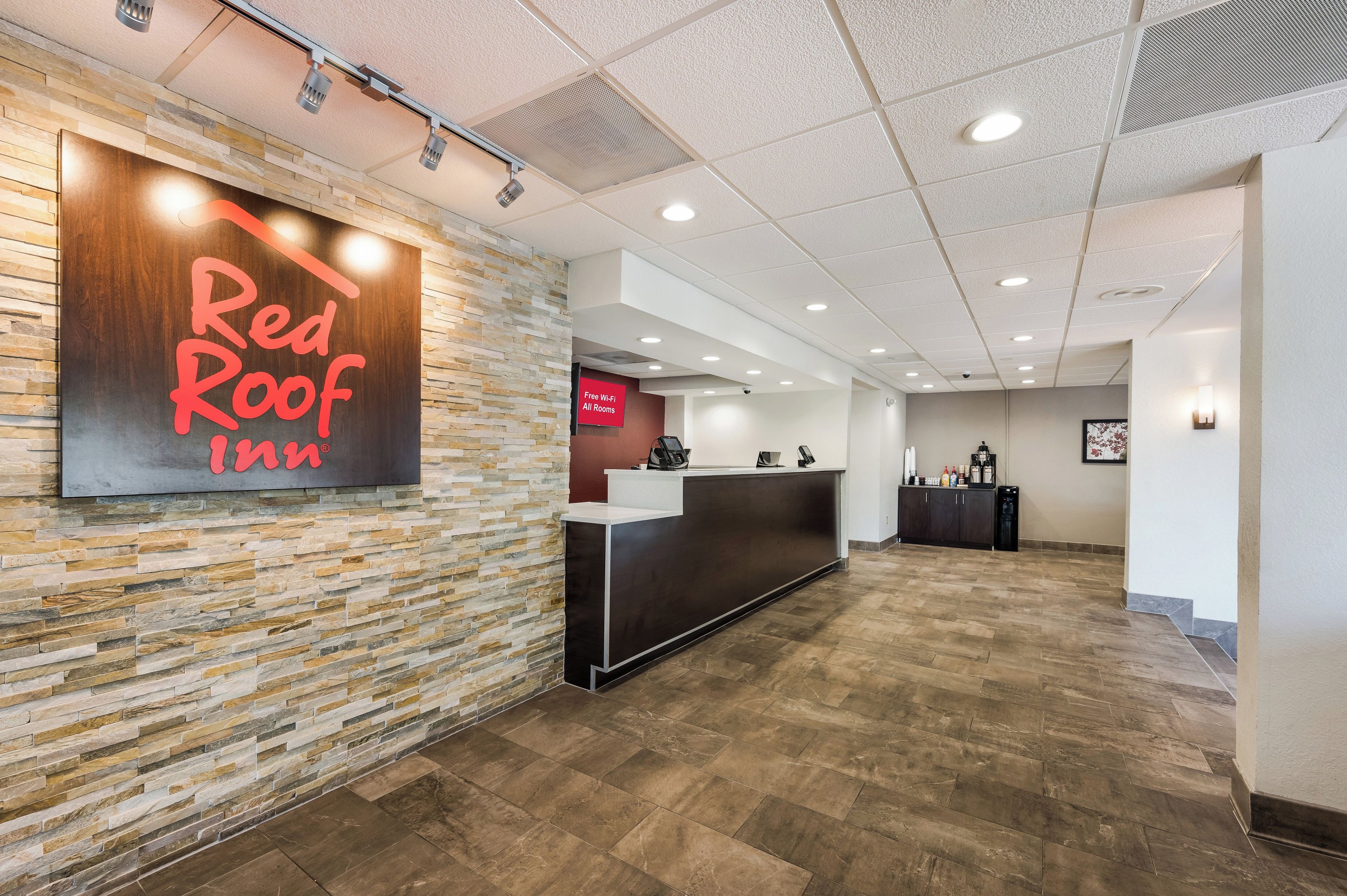 A reception area with a stone wall, a Red Roof Inn sign, a reception desk, and a 'Free Wi-Fi All Rooms' sign.