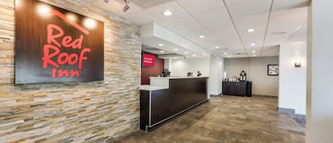 A reception area with a stone wall, a Red Roof Inn sign, a reception desk, and a 'Free Wi-Fi All Rooms' sign.