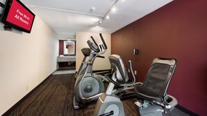 A gym with exercise equipment, a TV displaying 'Free Wi-Fi All Rooms', and a mirror in the background. - Red Roof Inn Birmingham South (Birmingham)