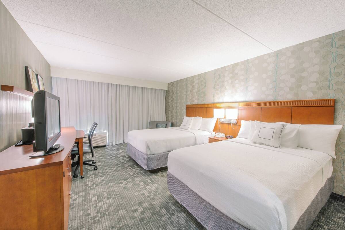 A hotel room with two beds, a desk with a computer, and a TV.