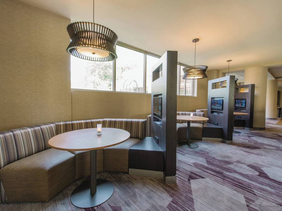 Een moderne hotel lobby met een gebogen zithoek, een ronde tafel en een televisiescherm.